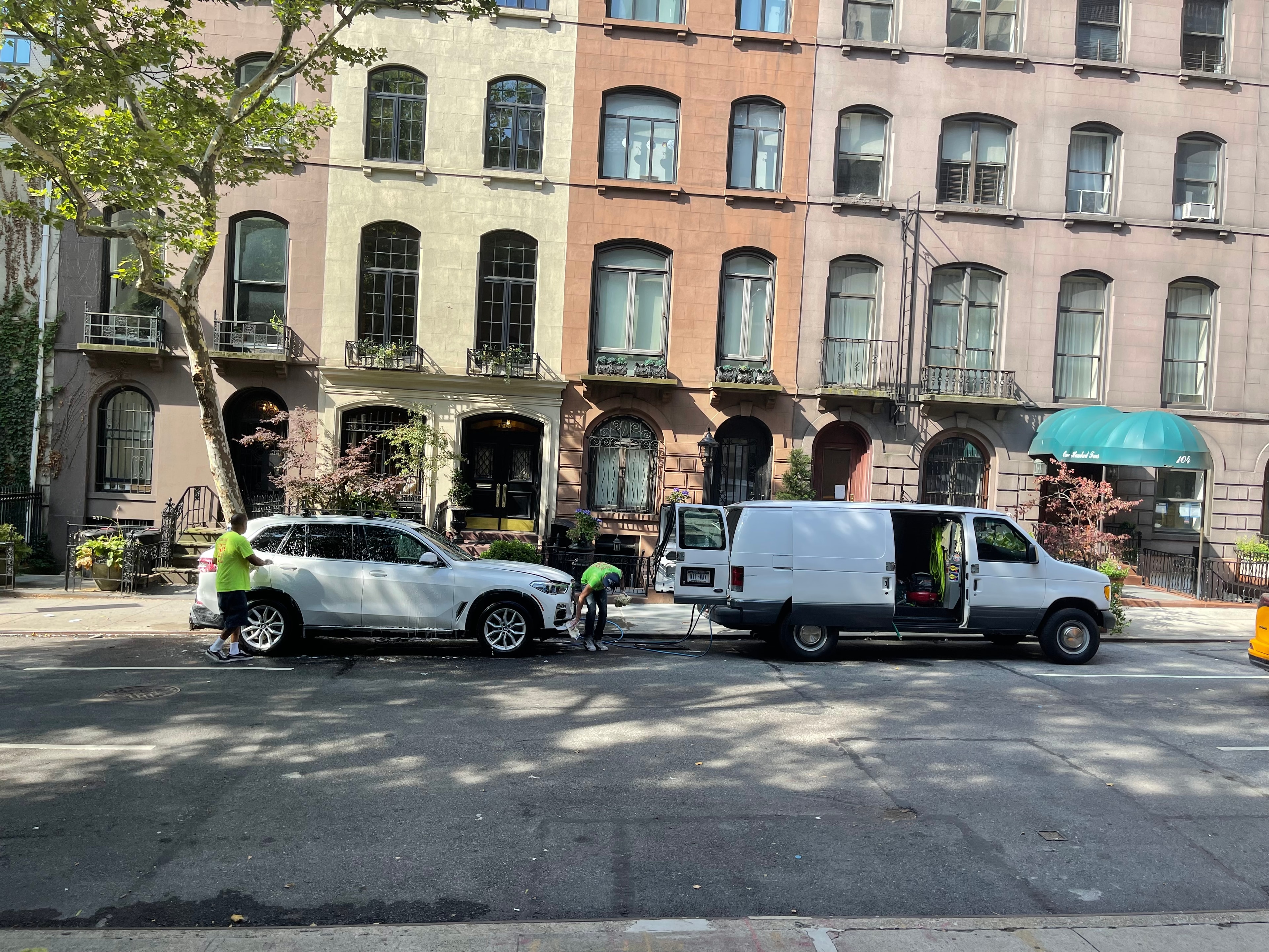 Wilson Waxes crew detailing a white BMW X5 on a Manhattan brownstone block