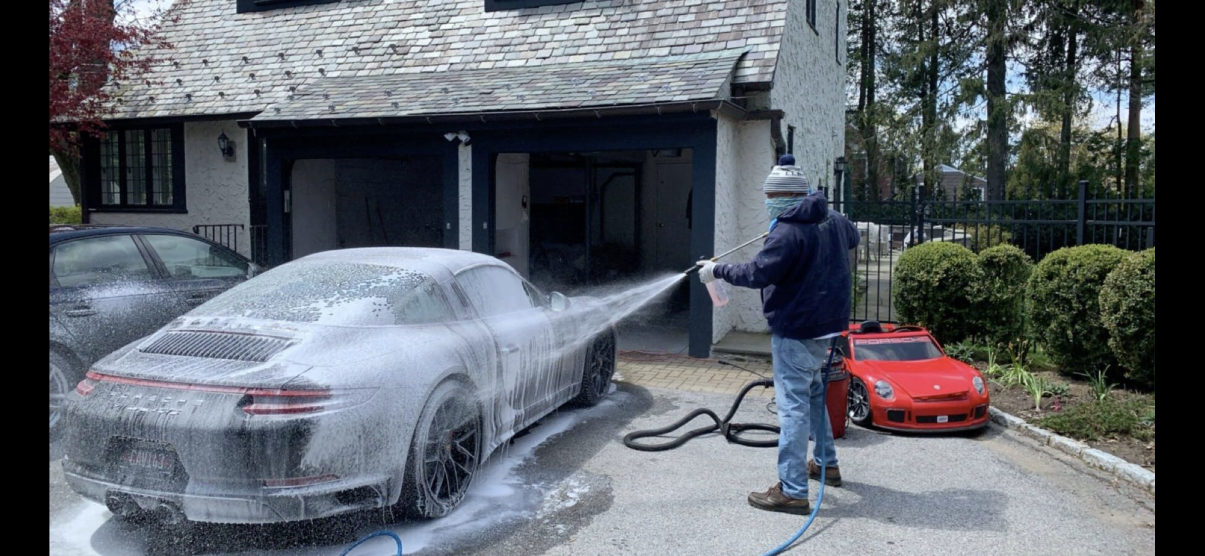 Wilson Waxes technician pressure washing a Porsche 911 in a residential driveway